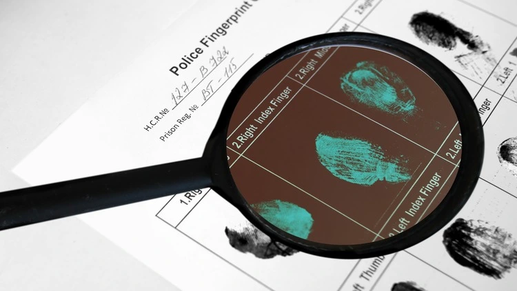 An image showing a magnifying glass placed over a police fingerprint form, revealing the magnified fingerprint impressions on the form.