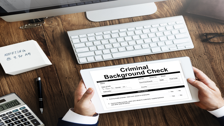 A person holding a criminal background check form on a desk with a computer keyboard, calculator, and a note pad.