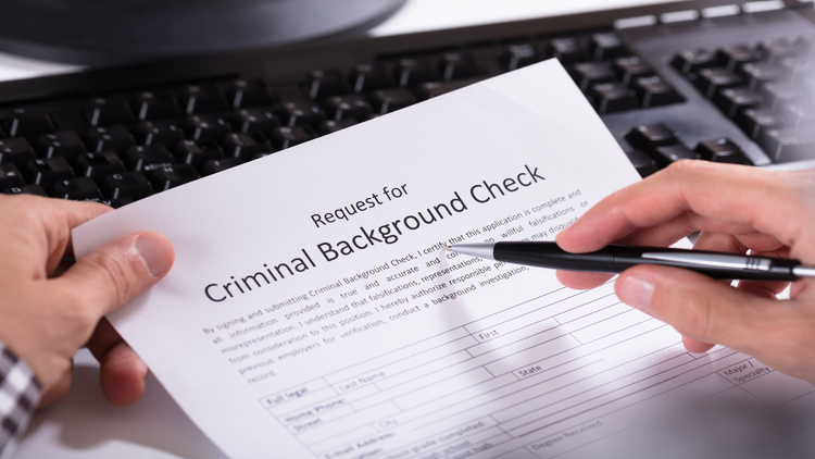 An image showing a person's hands filling out a request for a criminal background check form on a keyboard.