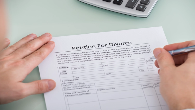 An image showing a Petition for Divorce form, with hands holding the document and a calculator visible in the background.