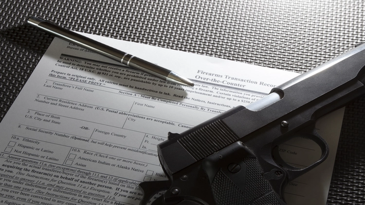 An image showing a pen and a handgun resting on top of a firearms transaction record form.