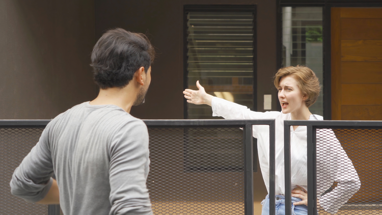 An image showing an argument or confrontation between two people, with one person gesturing at the other through a mesh screen or barrier.