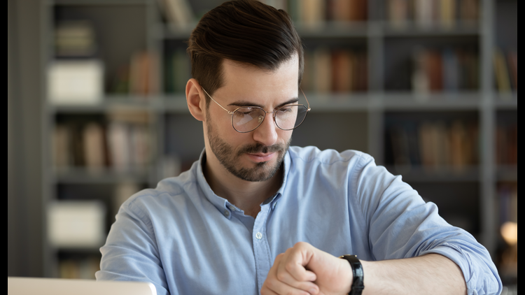 Man wearing glasses looking at his wristwatch in a library.