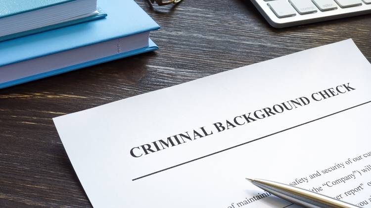 Criminal background check document on a wooden desk with books, calculator, and pen