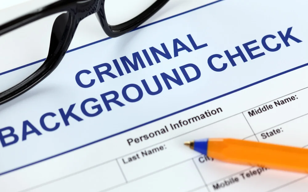 Criminal background check form, black glasses at the top and blue pen pointing to personal information. 