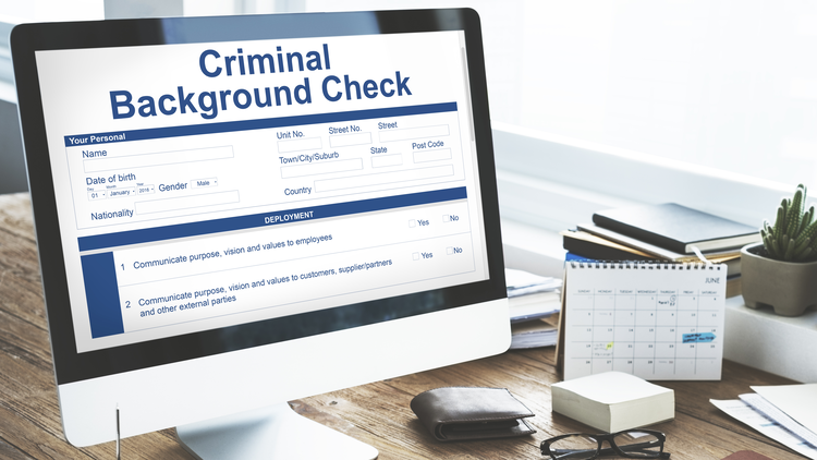 Computer screen showing criminal background check form on a desk with a calendar beside it depicting a delayed background check.