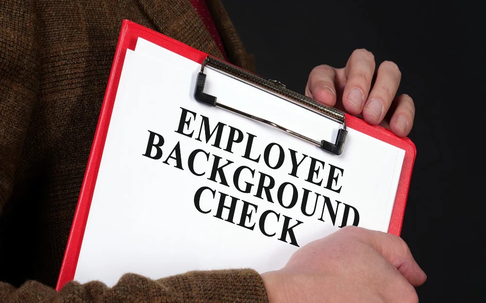 Man holding an employee background check form held by red clipboard. 