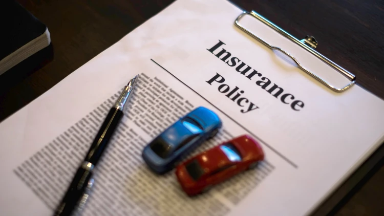 Close-up view of an insurance policy document on a clipboard with a pen and two toy cars on top.
