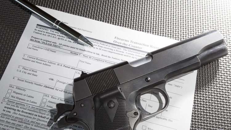 Image of a pen and handgun with documents required to purchase the gun. 