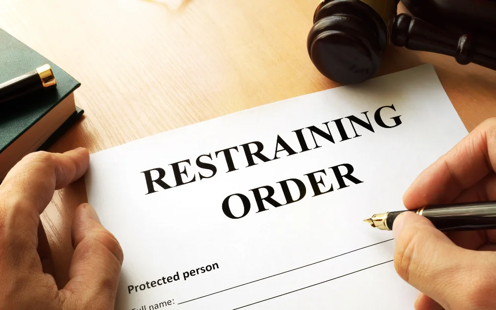 Restraining order form being filled out on a bench with a judges gavel in the upper right corner and the person to be protected name being filled in. 