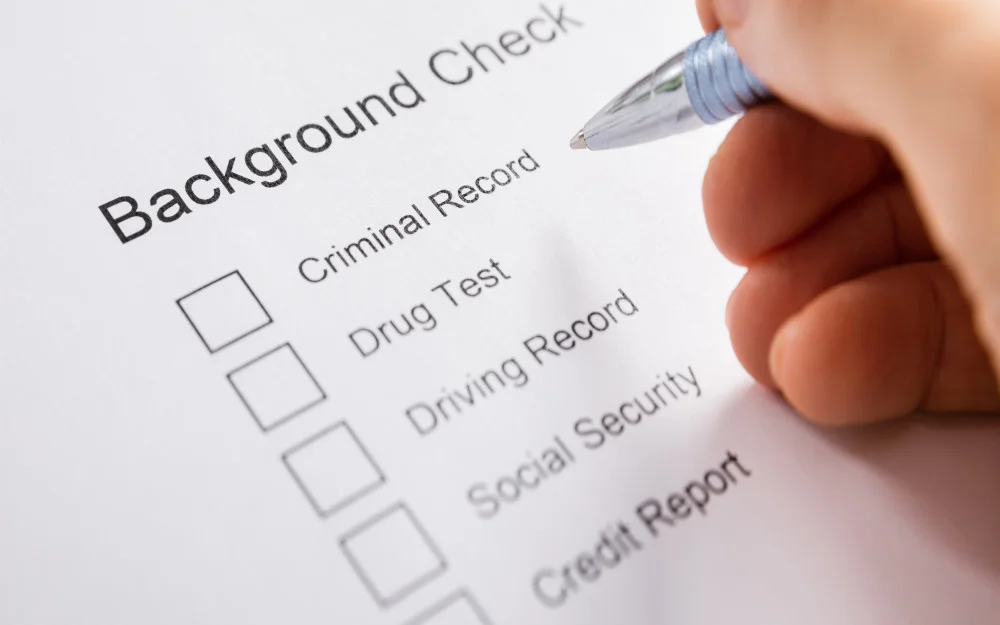 List of things that can be on a background check with a person holding a pen above the blank check boxes beside the list. 