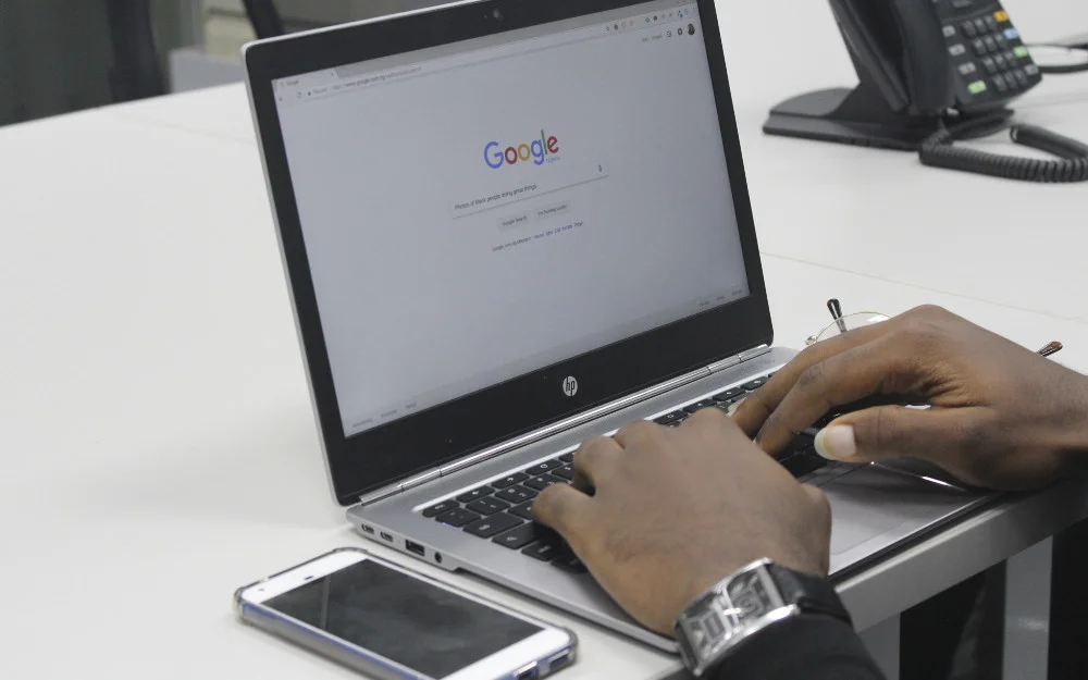 Man using google search on a laptop with a phone beside it to know how to find someone's middle name. 