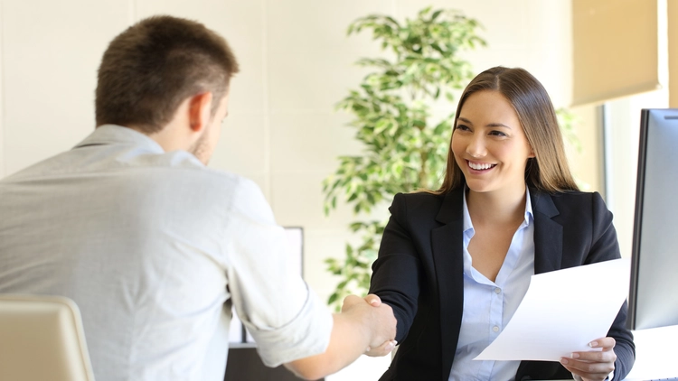 A job interviewer shaking hands with an applicant in an office setting.
