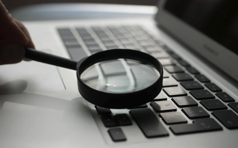 Magnifying glass laid on a computer keyboard to represent an online search of how to find out where someone works. 