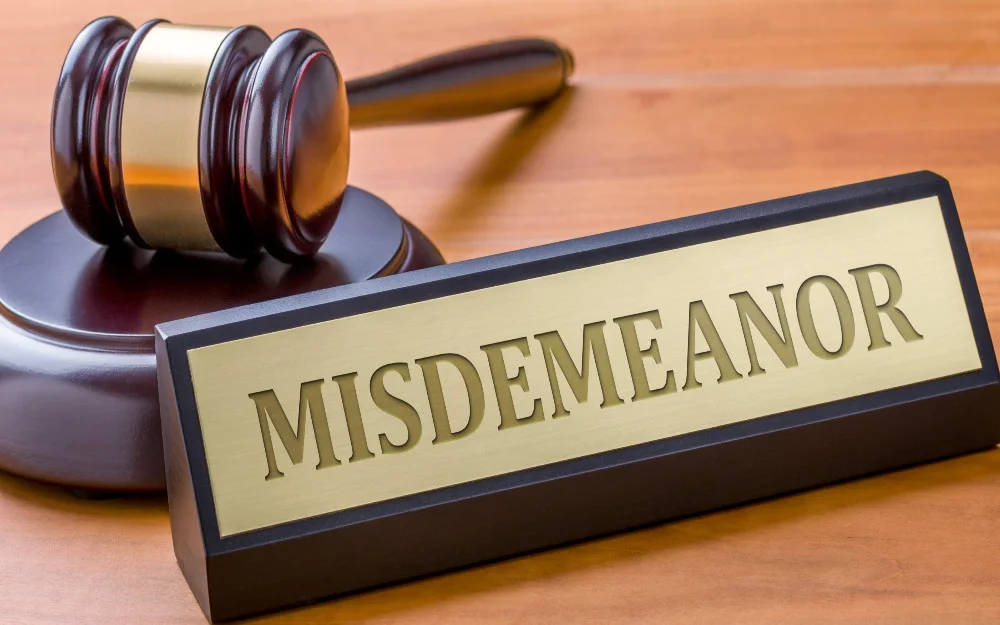 Gavel on a wooden desk, with a name plate with the word misdemeanor on it. 