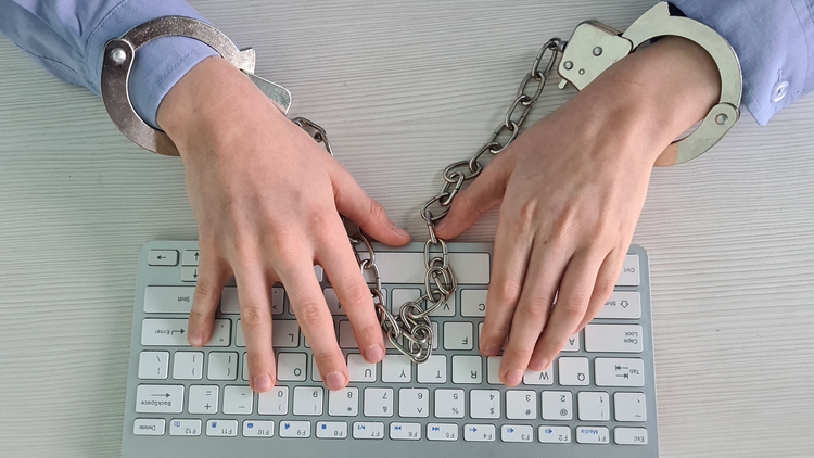 Image of hands with handcuffs on a keyboard.