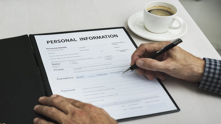 Person filling out personal information form with coffee nearby.