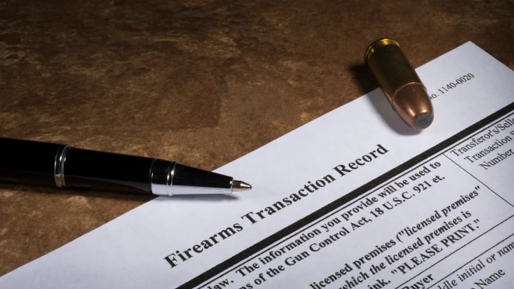 Close-up view of a firearms transaction record form with a pen and a bullet on top.