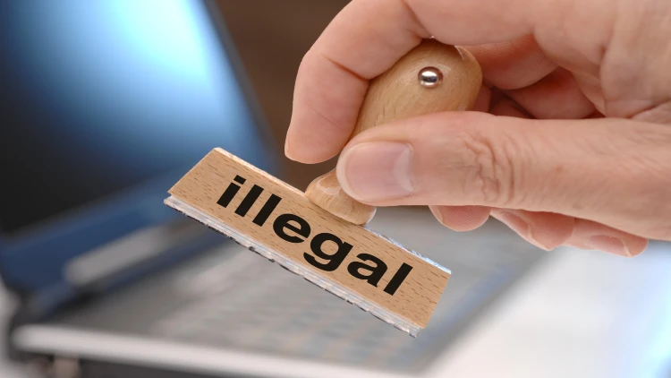 Close-up of man's hand holding rubber stamp with wooden handle, stamped with the word 'illegal'.