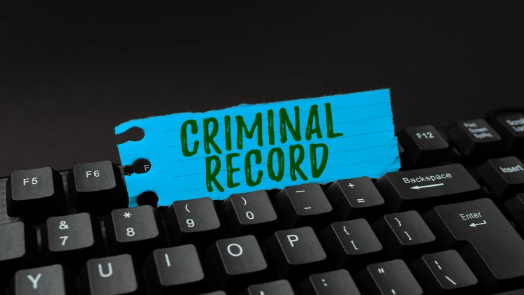 Close-up of a QWERTY keyboard with a paper inserted between the keys, displaying the words 'criminal record'.
