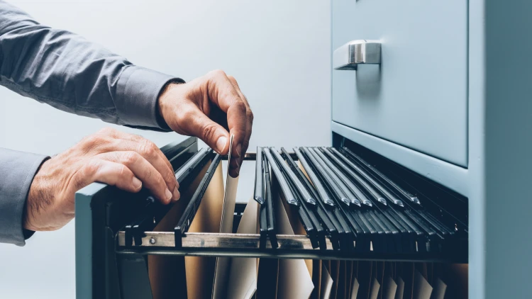 Man's hand holding a folder in an open filing cabinet.