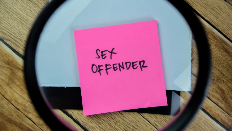 Pink sticky note with the words 'sex offender' written on it under a magnifying glass.