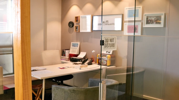 A glass door with a 'Do Not Disturb' sign opens to an office with a desk, two chairs, and framed pictures on the wall, hinting at an abandoned job.
