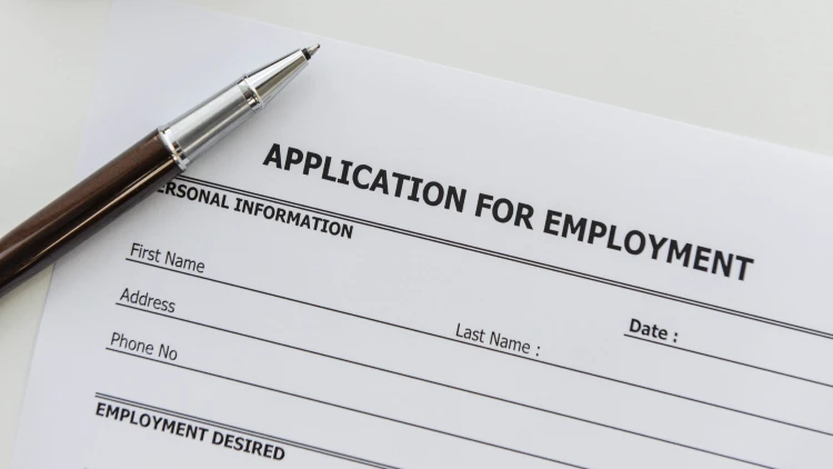 Close-up view of an employment application form with a ballpoint pen resting on top.