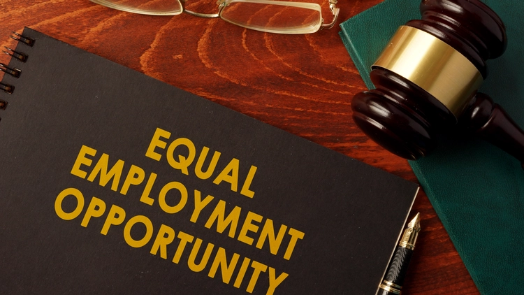 Book with title "Equal Employment Opportunity" next to judge's gavel and glasses on wooden table.