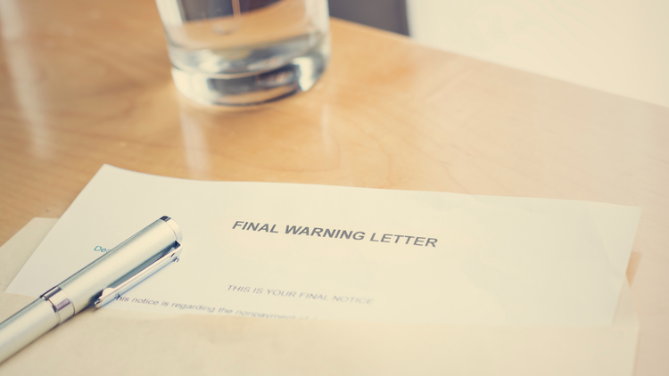 A final warning letter with a pen placed next to it on a wooden table, and a glass of water in the background.