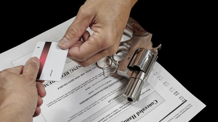Close-up view of two hands holding one card with a gun and some paper documents underneath.