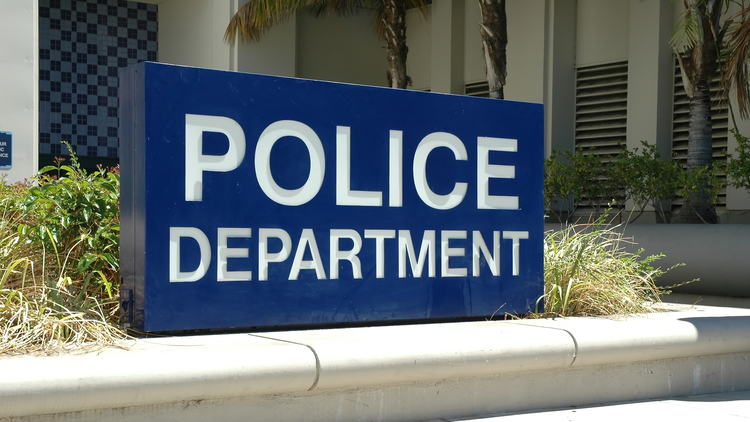 A Police Department sign that reads in front of a building with palm trees in the background.