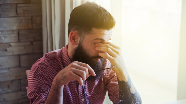 A troubled man with a beard covers his face, likely due to challenges from a criminal record affecting his employment.