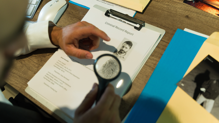 A person examining a criminal record report with a magnifying glass.