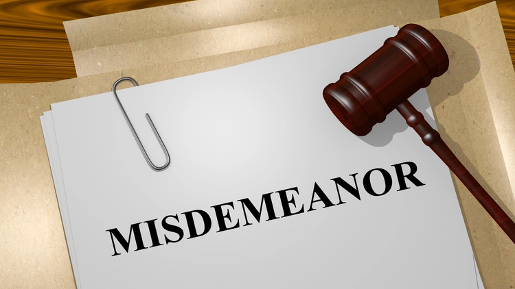 A closeup shot depicting a gavel resting on top of a white sheet of paper that has the word "misdemeanor" printed on it.