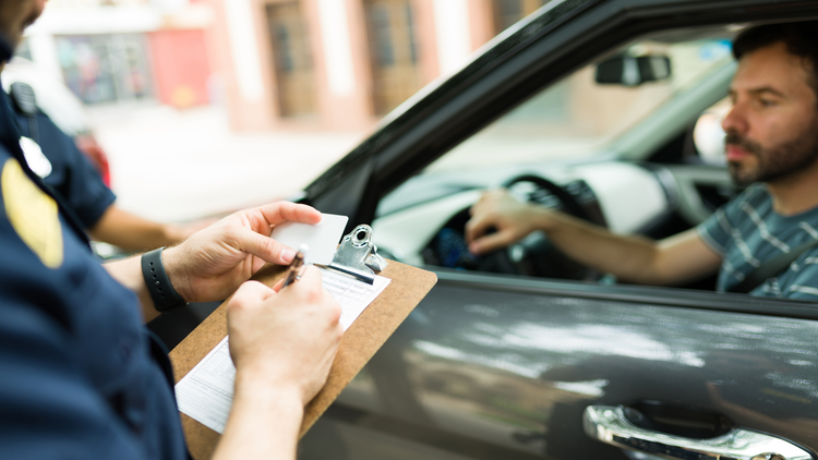 Close up image of a police officer writing a traffic ticket to a male driver.