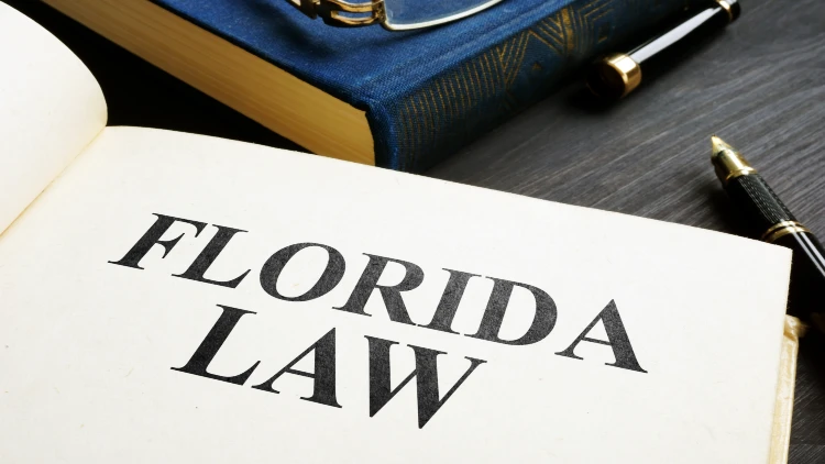 Close up image of Florida law text on an open book on top of a desk with a pen beside it.