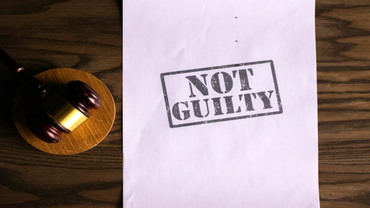 Image of a not guilty print beside a gavel and pound on top a desk top