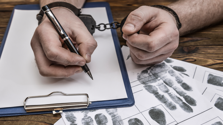 Hands of a person taking fingerprints on a clipboard with documents, representing criminal arrest.