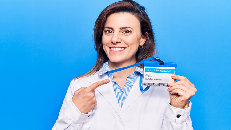 A smiling woman in a medical uniform holding a hospital identification badge.