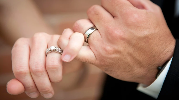 Close up image of two hands wearing wedding rings having their little finger hooked together