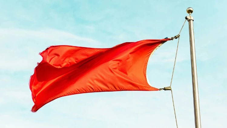 Image of red flag raised and being blown by the wind