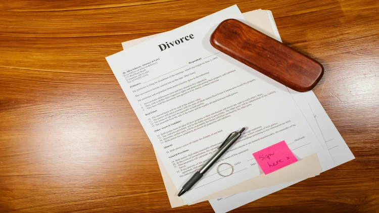 Image of divorce papers with a note that says sign here and a pen and a ring on top