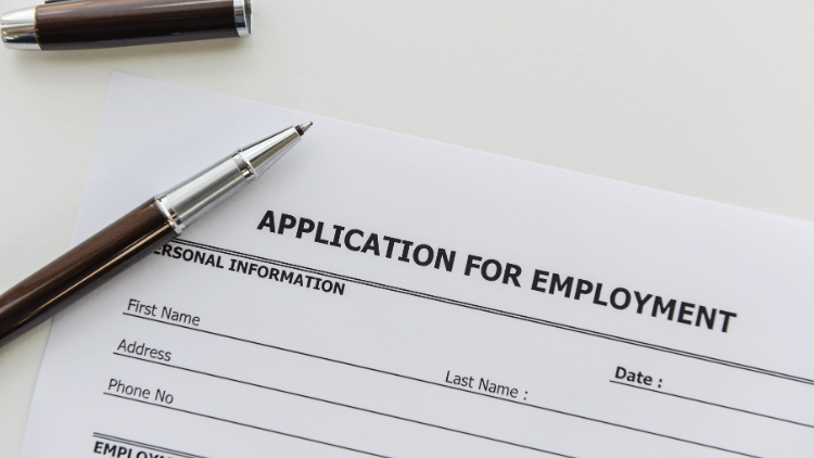 Close-up view of an employment application form with a ballpoint pen resting on top.