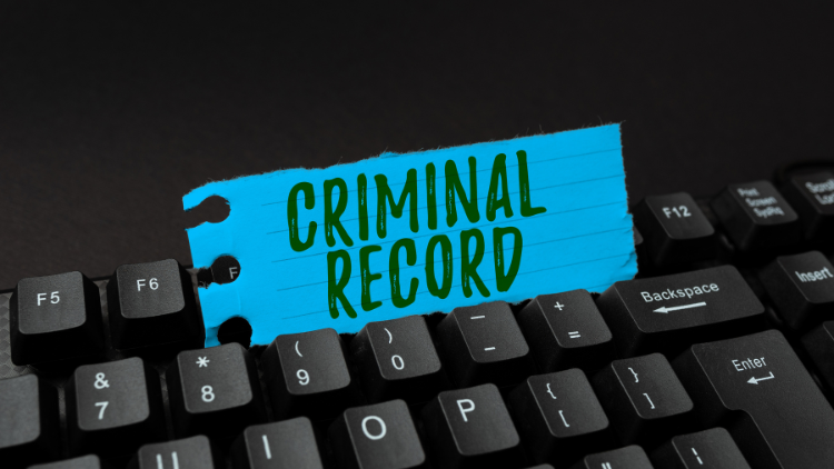 Close-up of a QWERTY keyboard with a paper inserted between the keys, displaying the words 'criminal record'.