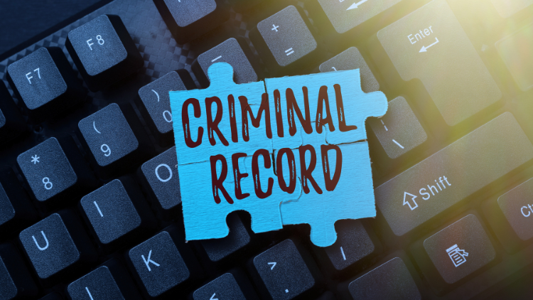A blue puzzle piece with "CRIMINAL RECORD" written on it is placed on a black computer keyboard.