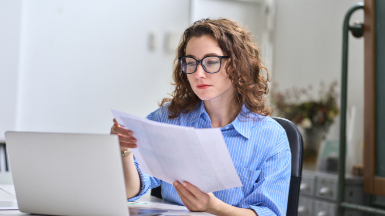 A woman by her desk holding and reviewing documents.