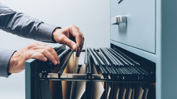 Man's hand holding a folder in an open filing cabinet.