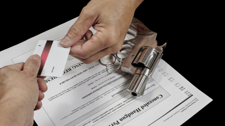 Close-up view of two hands holding one card with a gun and some paper documents underneath.