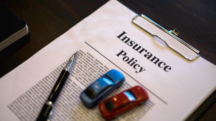 Close-up view of an insurance policy document on a clipboard with a pen and two toy cars on top.